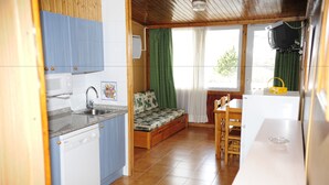 Uma cozinha compacta com micro-ondas, pia e armários de madeira. Uma pequena área de jantar com mesa e cadeiras fica adjacente à cozinha.