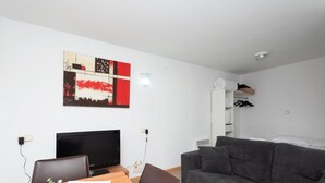 Uma sala de estar moderna com uma televisão de tela plana, uma mesa de jantar de madeira, um sofá cinza e uma pintura abstrata pendurada na parede.