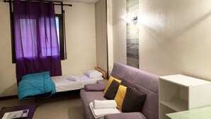 Quarto pequeno e compacto com cama, sofá e uma mesinha.