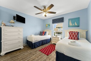 Un dormitorio con dos camas, ventilador de techo, cómoda y televisor.