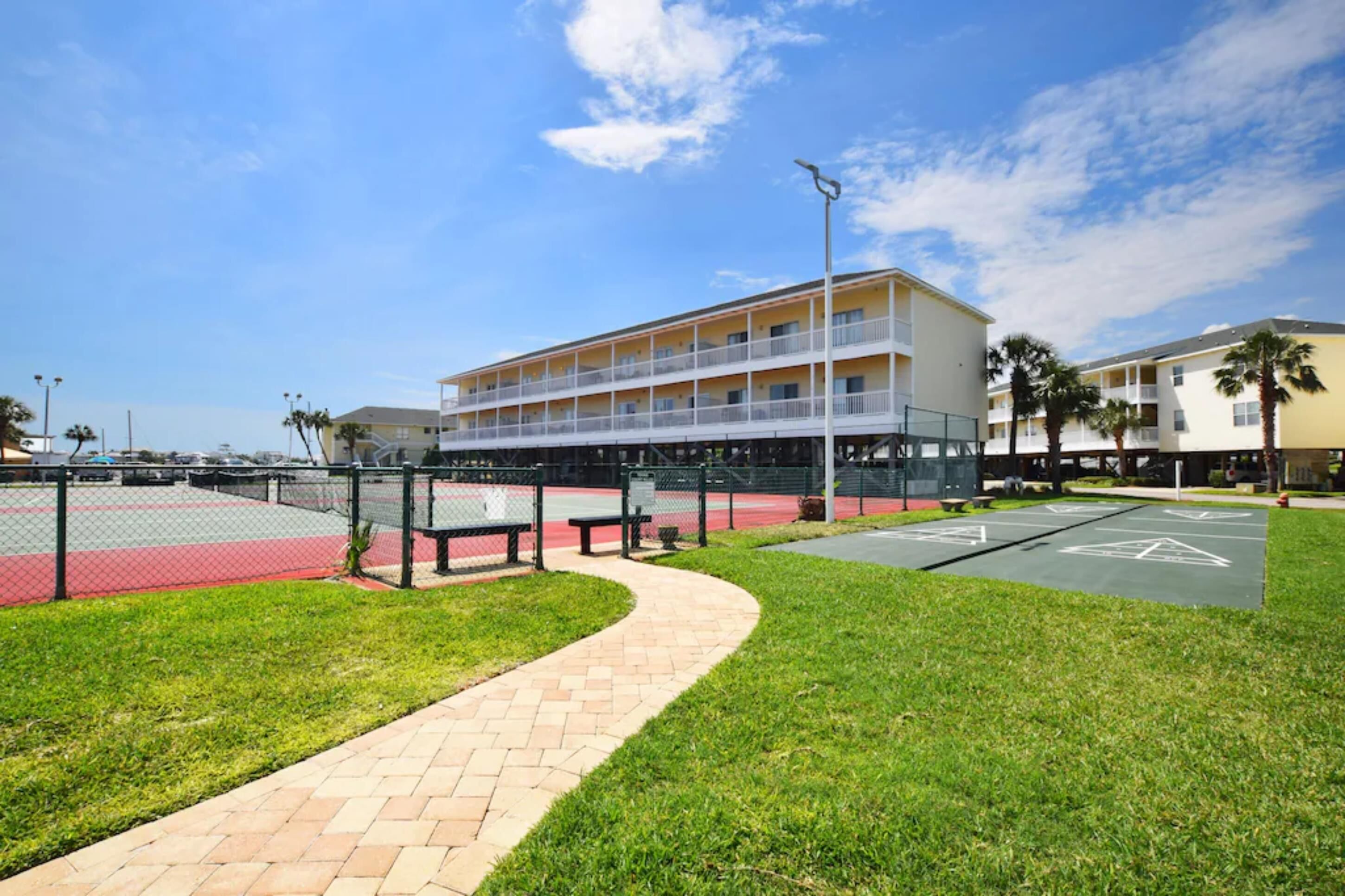 A multi-story hotel with a balcony on the second floor, a parking lot, and a grassy area with a pathway.