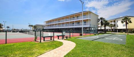 A multi-story hotel with a balcony on the second floor, a parking lot, and a grassy area with a pathway.