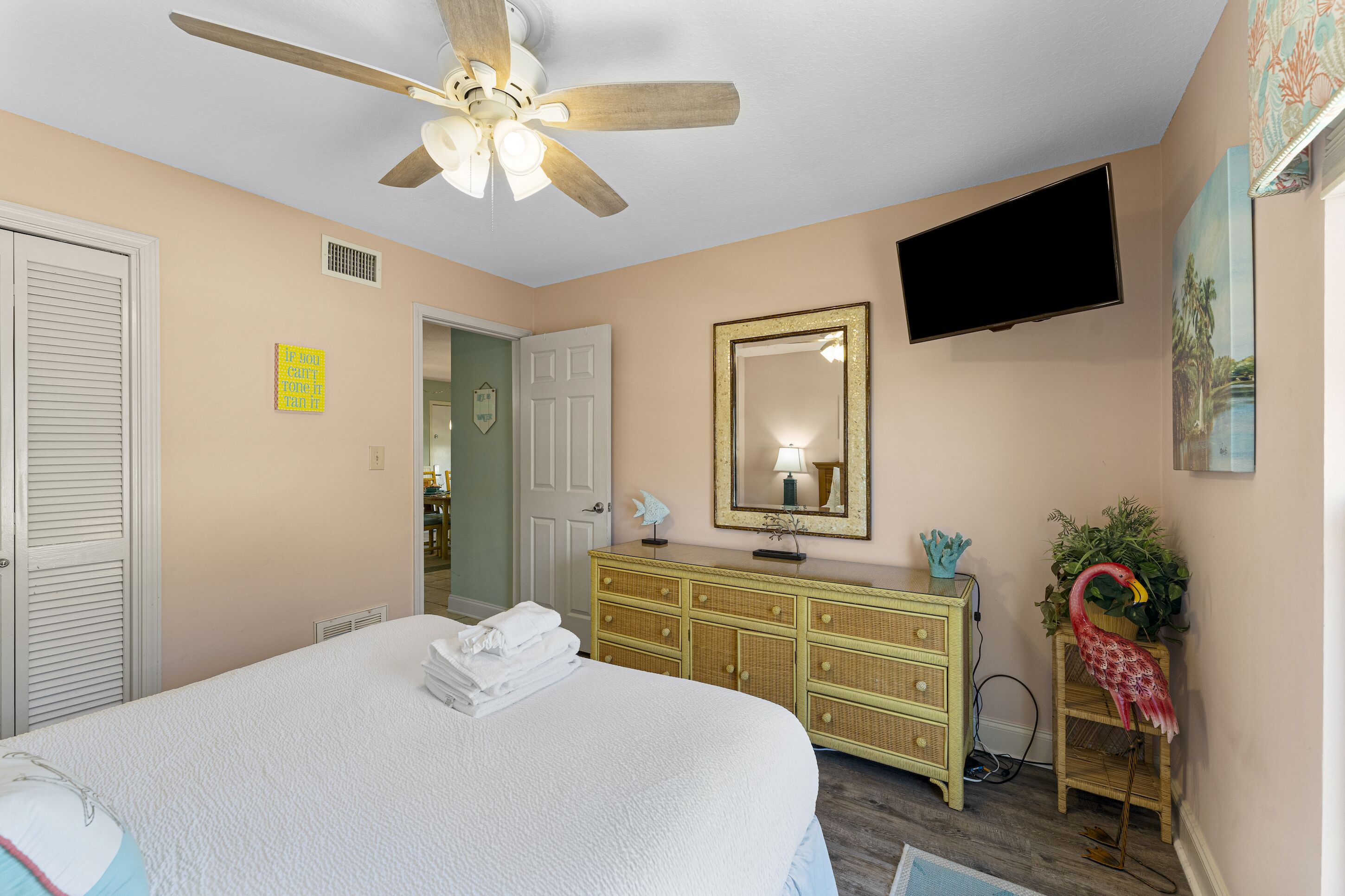 A bedroom with a bed, a ceiling fan, a dresser, a mirror, a television, and a door.