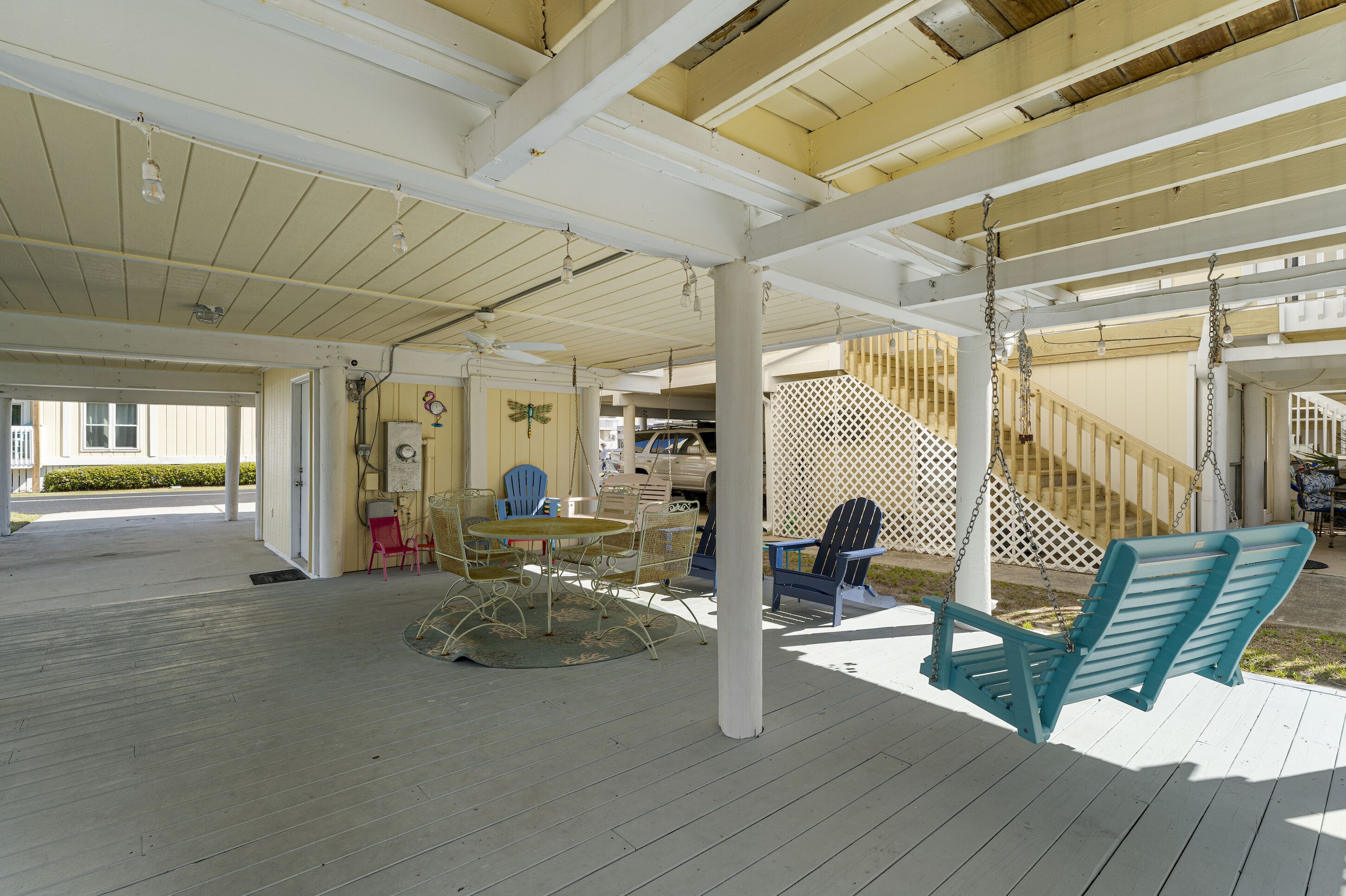 Un espace extérieur abrité doté d’une terrasse en bois, d’une balançoire et d’une table avec des chaises.