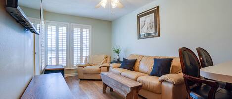 A living room with a wooden coffee table, a beige sofa, a dining table, and a ceiling fan.