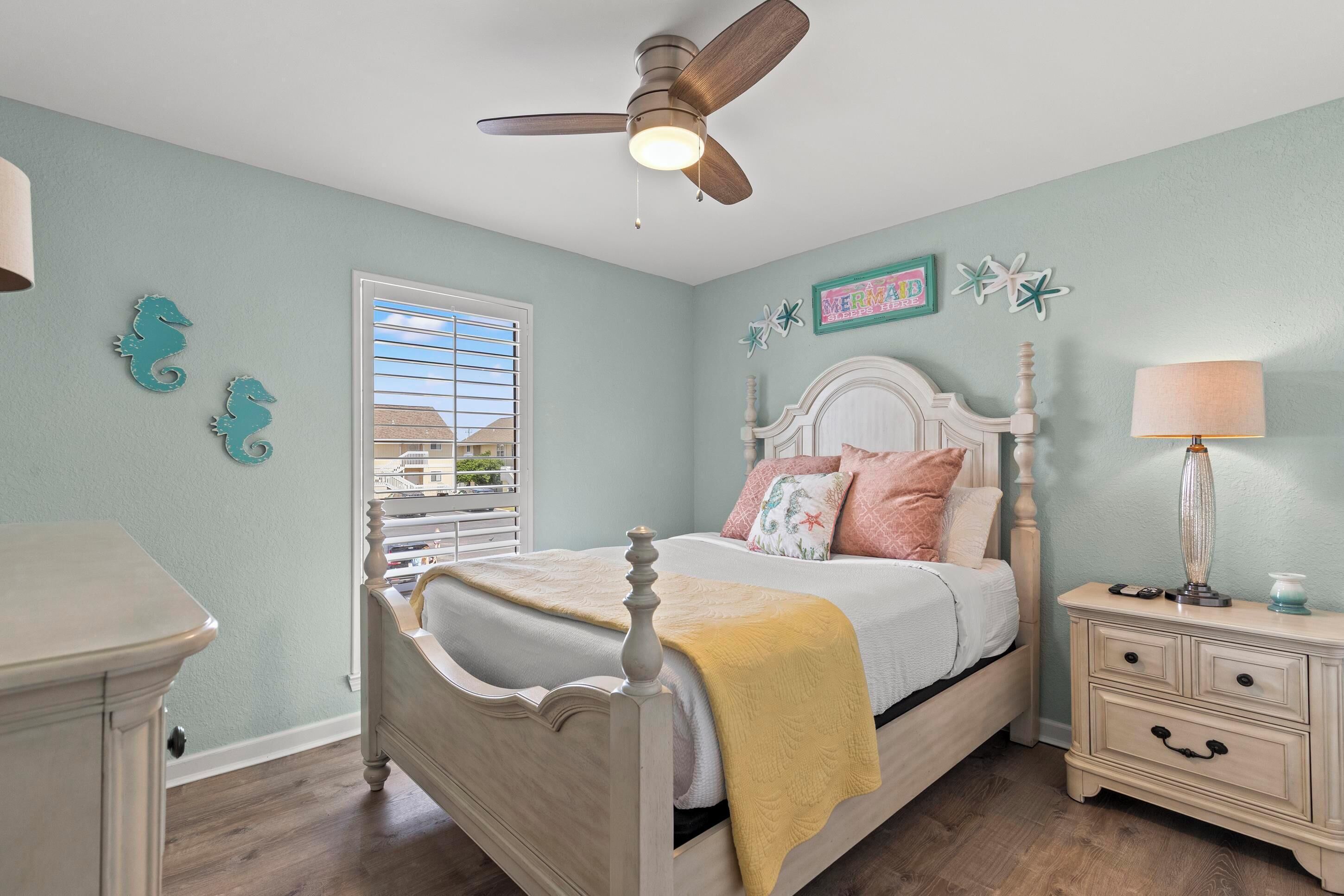 Un dormitorio con cama, mesita de noche, lámpara, ventilador de techo y decoración mural.