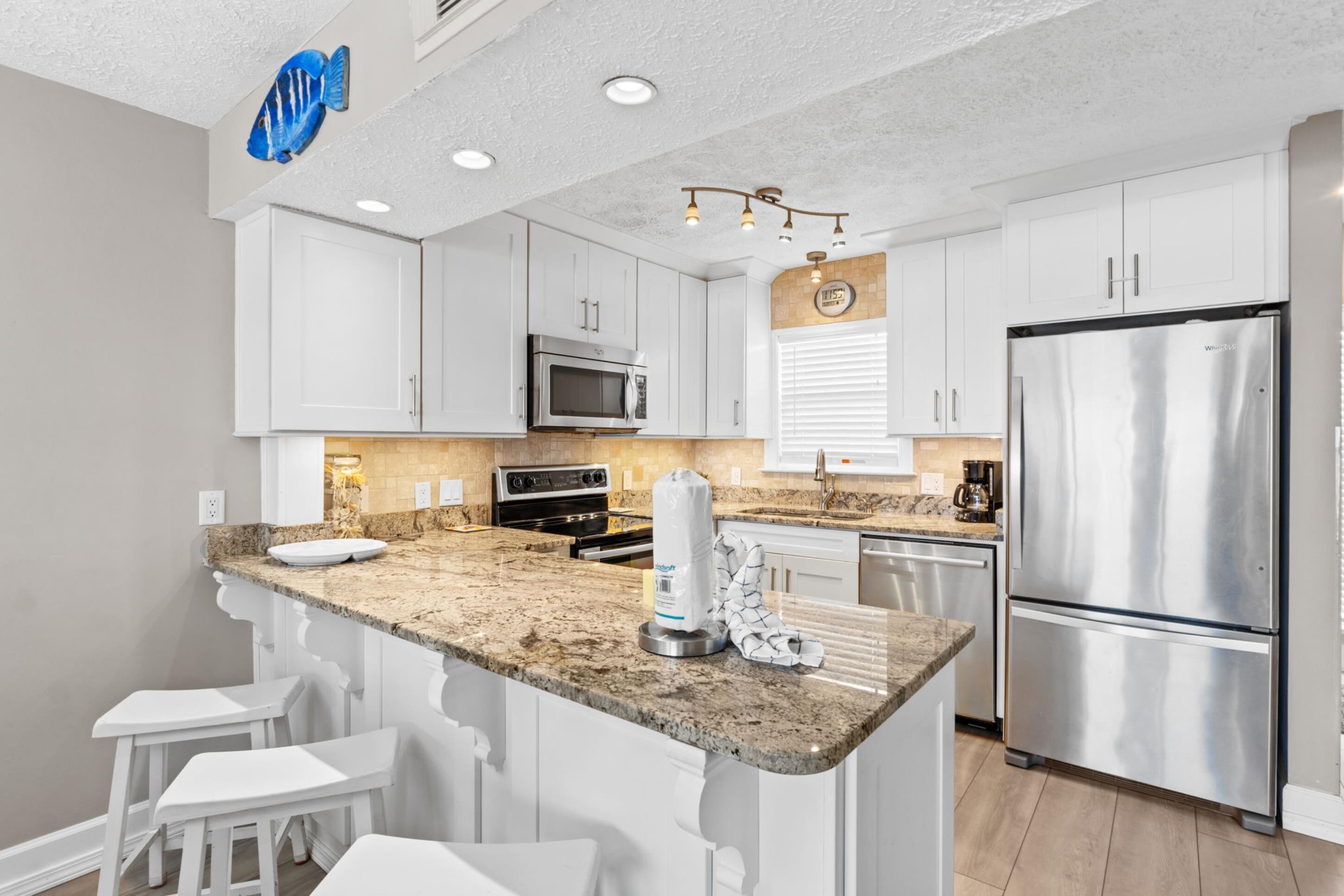 A kitchen with white cabinets, stainless steel appliances, a granite countertop, and a blue fish decoration.