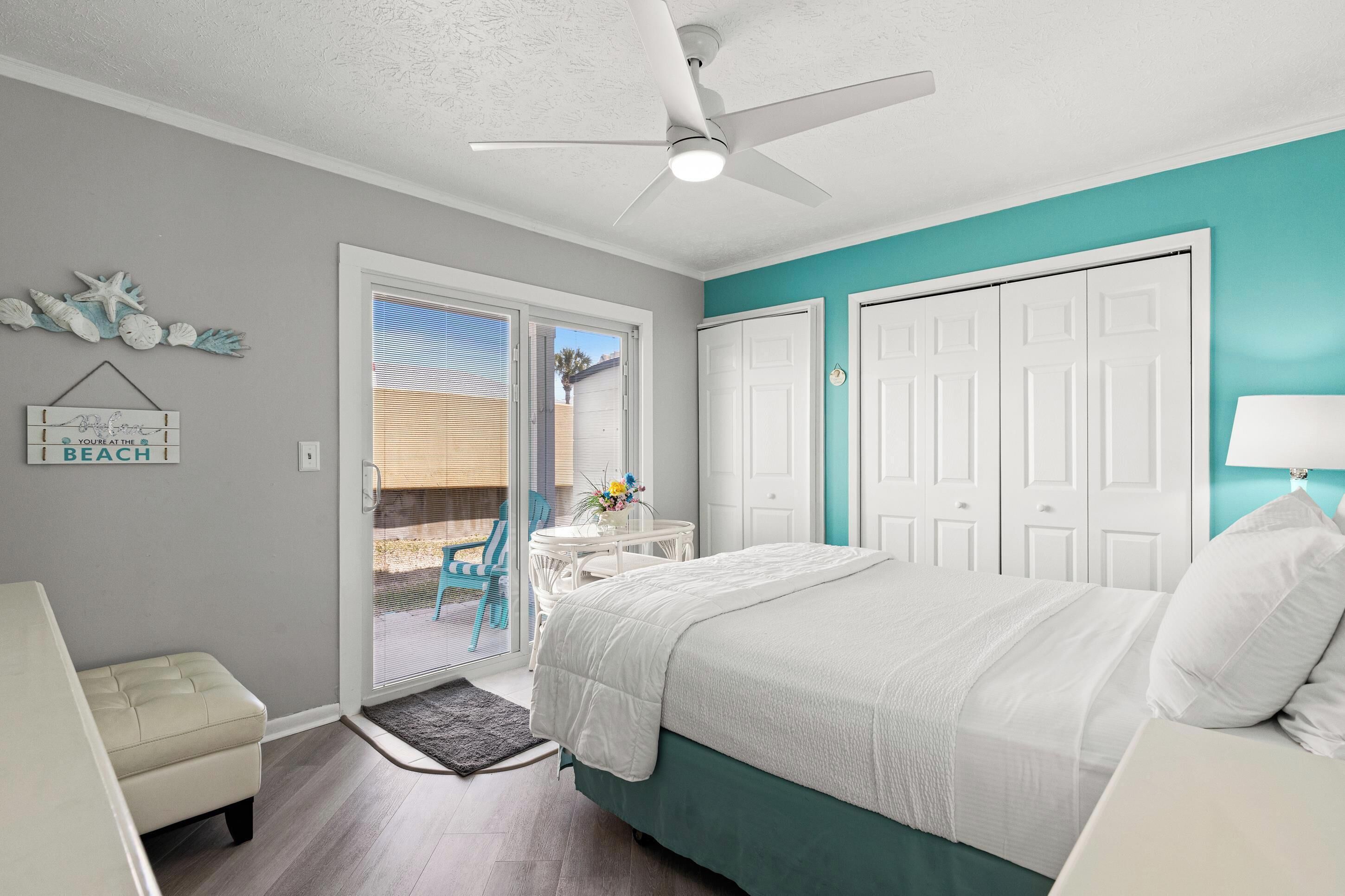 A bedroom with a bed, a ceiling fan, a sliding glass door to a patio, and a small table with chairs.