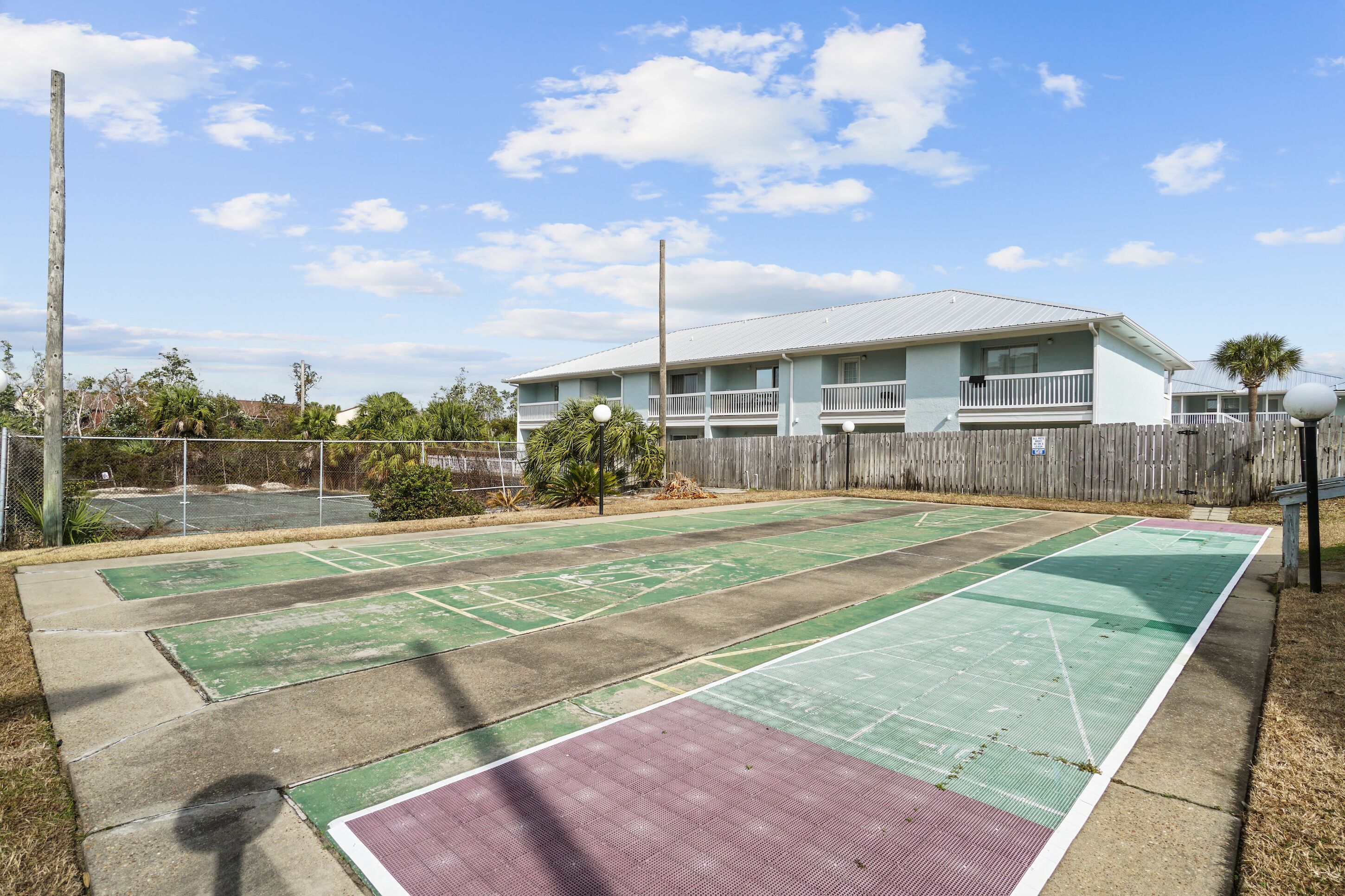 Un campo da tennis con una recinzione in legno e un edificio sullo sfondo.