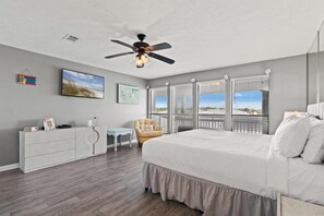 Une chambre à coucher comprenant un lit, un ventilateur de plafond, une commode, une chaise et une fenêtre avec des stores.