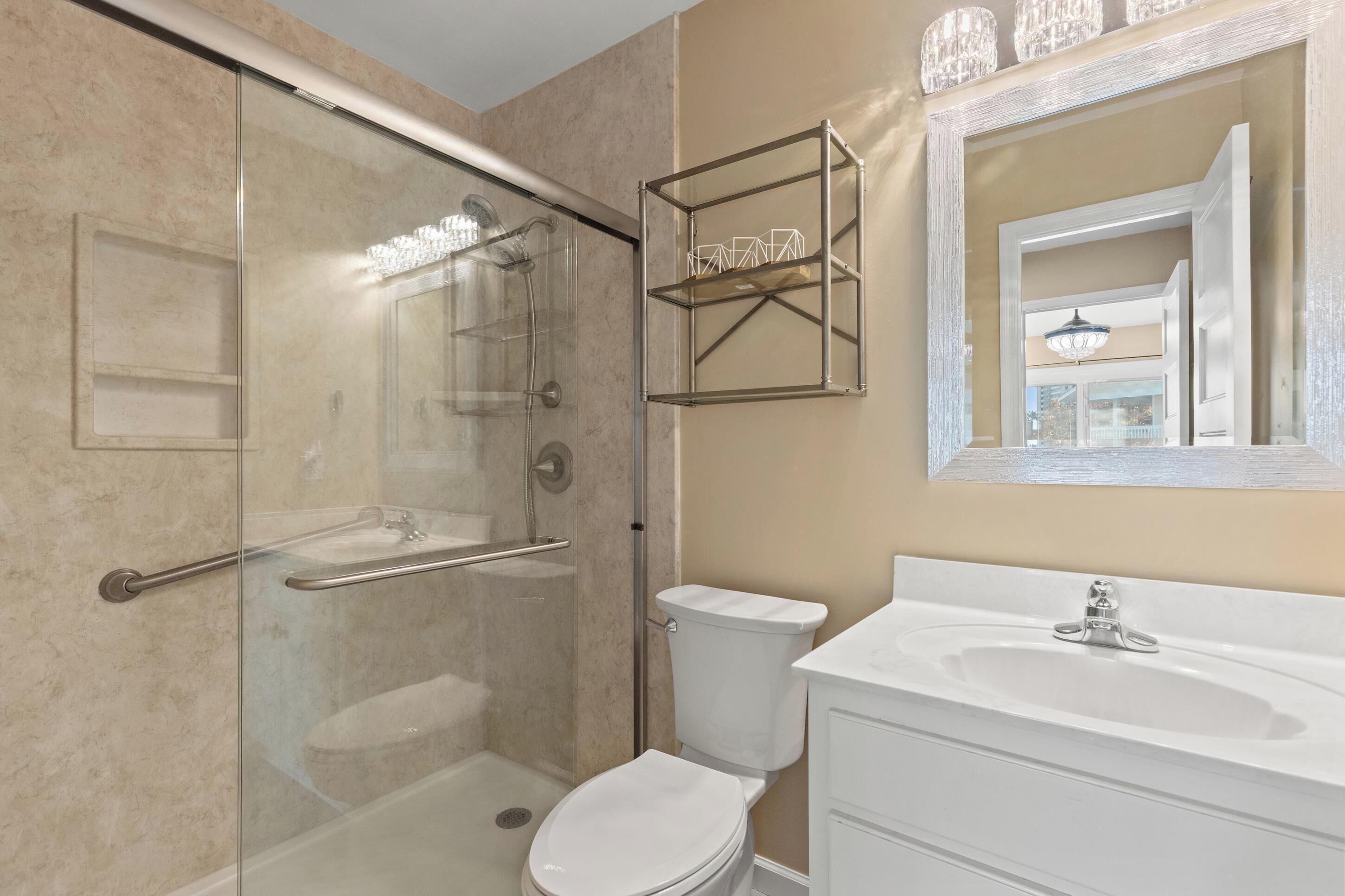 Une salle de bain avec une douche à parois de verre, des toilettes blanches, un lavabo blanc et un miroir doté d'un cadre décoratif.