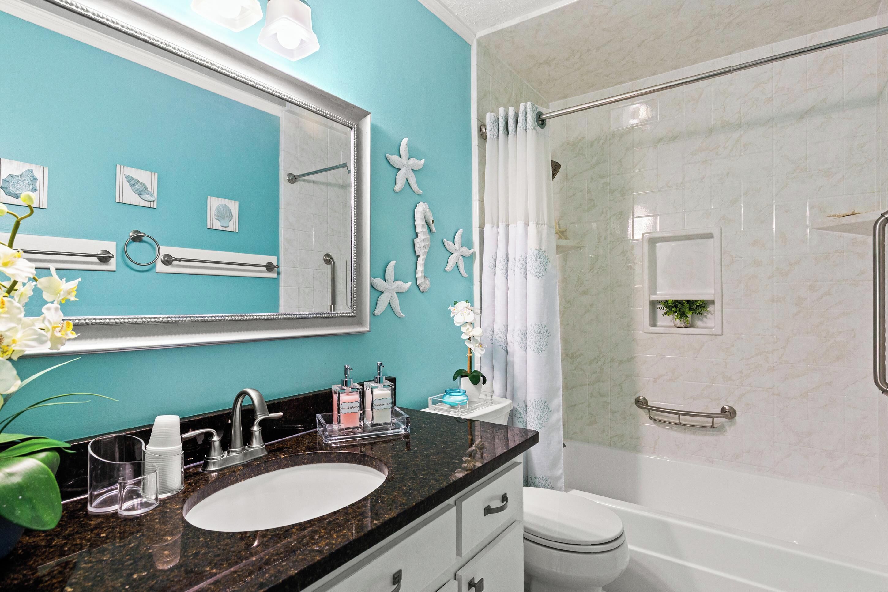 A bathroom with a turquoise wall, white fixtures, a sink, a toilet, and a shower with a glass door.
