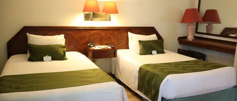 Une chambre d’hôtel avec deux lits simples, une table de chevet, un bureau avec une lampe et un miroir.