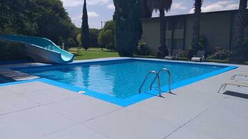 Una piscina con tobogán, rodeada de un solárium empedrado y palmeras.