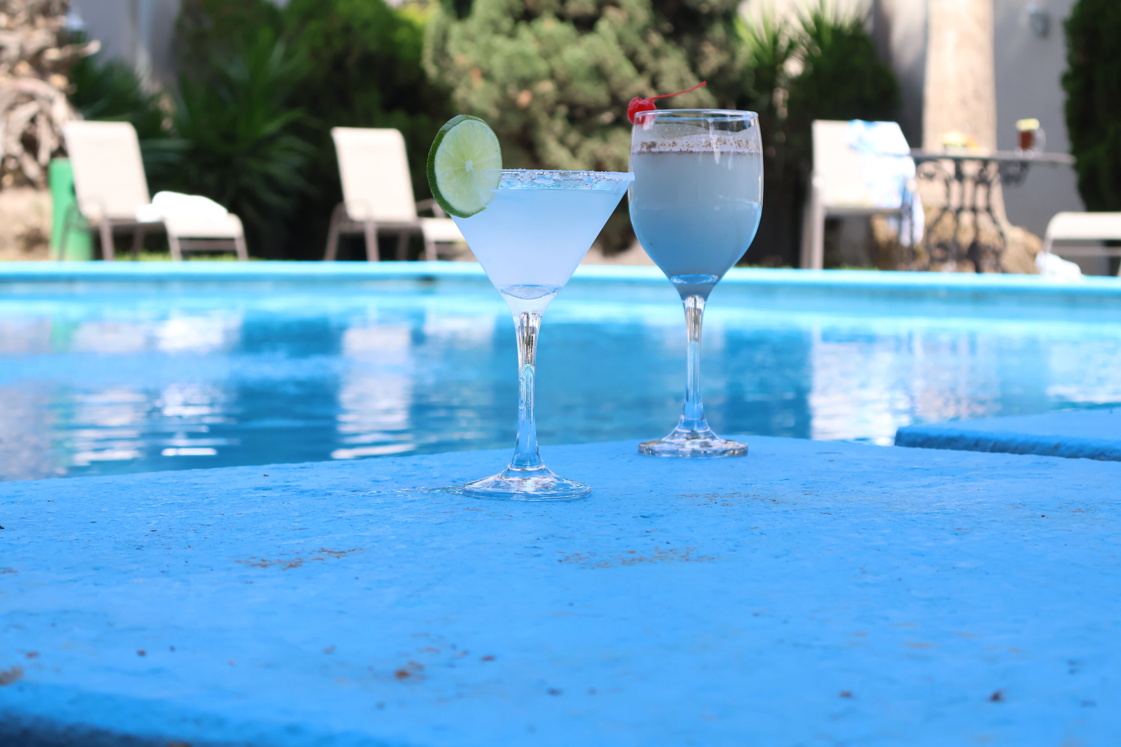 Dos vasos de agua sobre una superficie azul junto a una piscina.