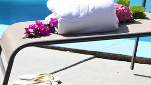 A poolside chair with a white towel and pink flowers, overlooking a clear blue pool.