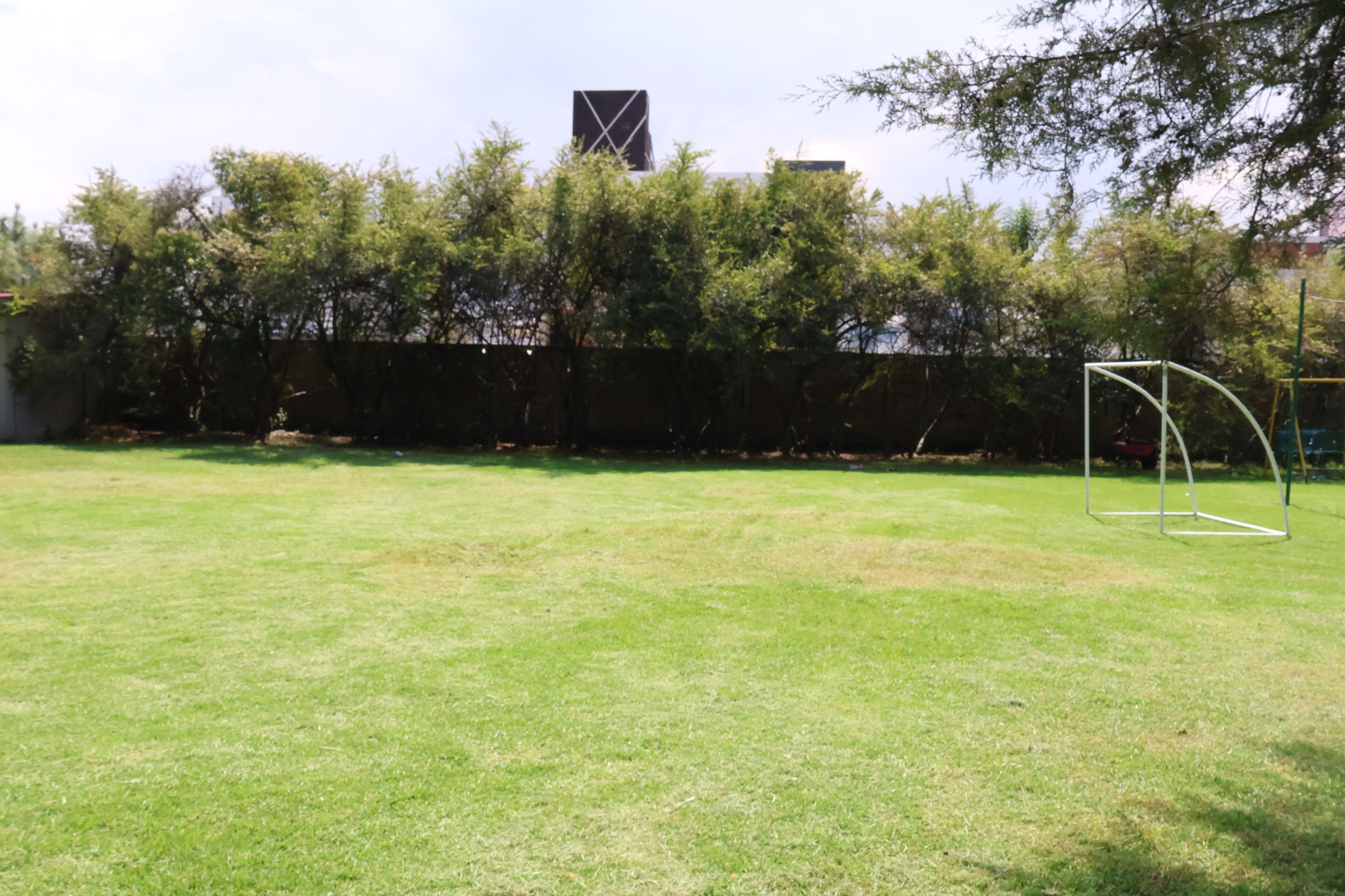 A grassy outdoor area with a goalpost, trees, and a building in the background.