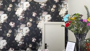 A reception desk with a floral wallpaper background, a vase with colorful flowers, a sign with check-in times, and a small plant. - Warfield Hotel (San Francisco)