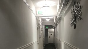A hallway with a patterned floor, white walls, and an exit sign. - Warfield Hotel (San Francisco)