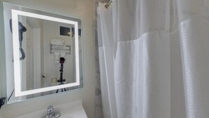 A bathroom with a large mirror, a sink, and a shower curtain. - Warfield Hotel (San Francisco)