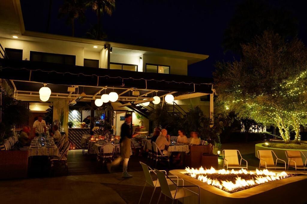 An outdoor dining area with tables and chairs, a fire feature, and string lights.
