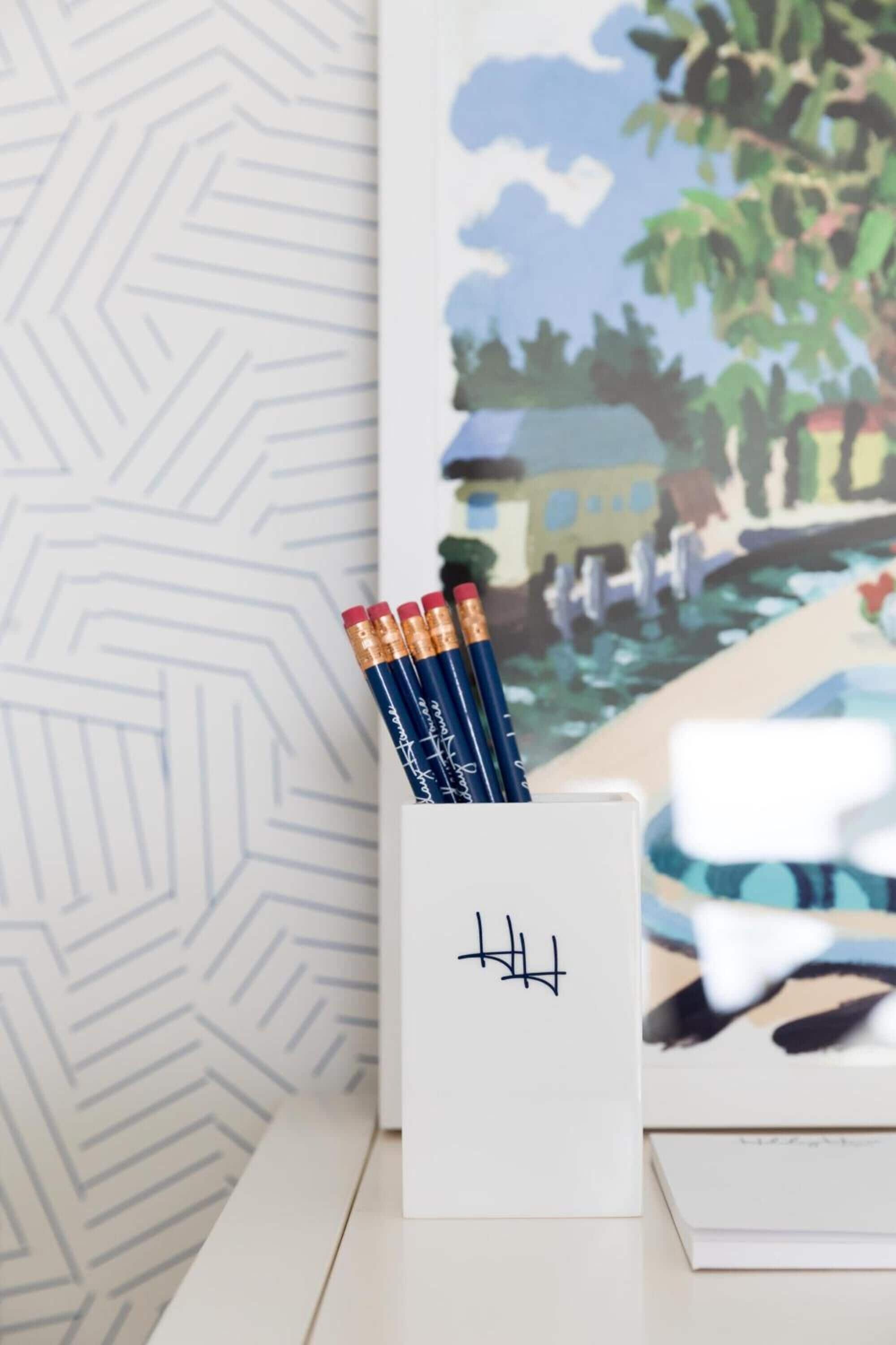 Uma escrivaninha com um bloco de notas branco, três lápis e um porta-canetas com design preto.