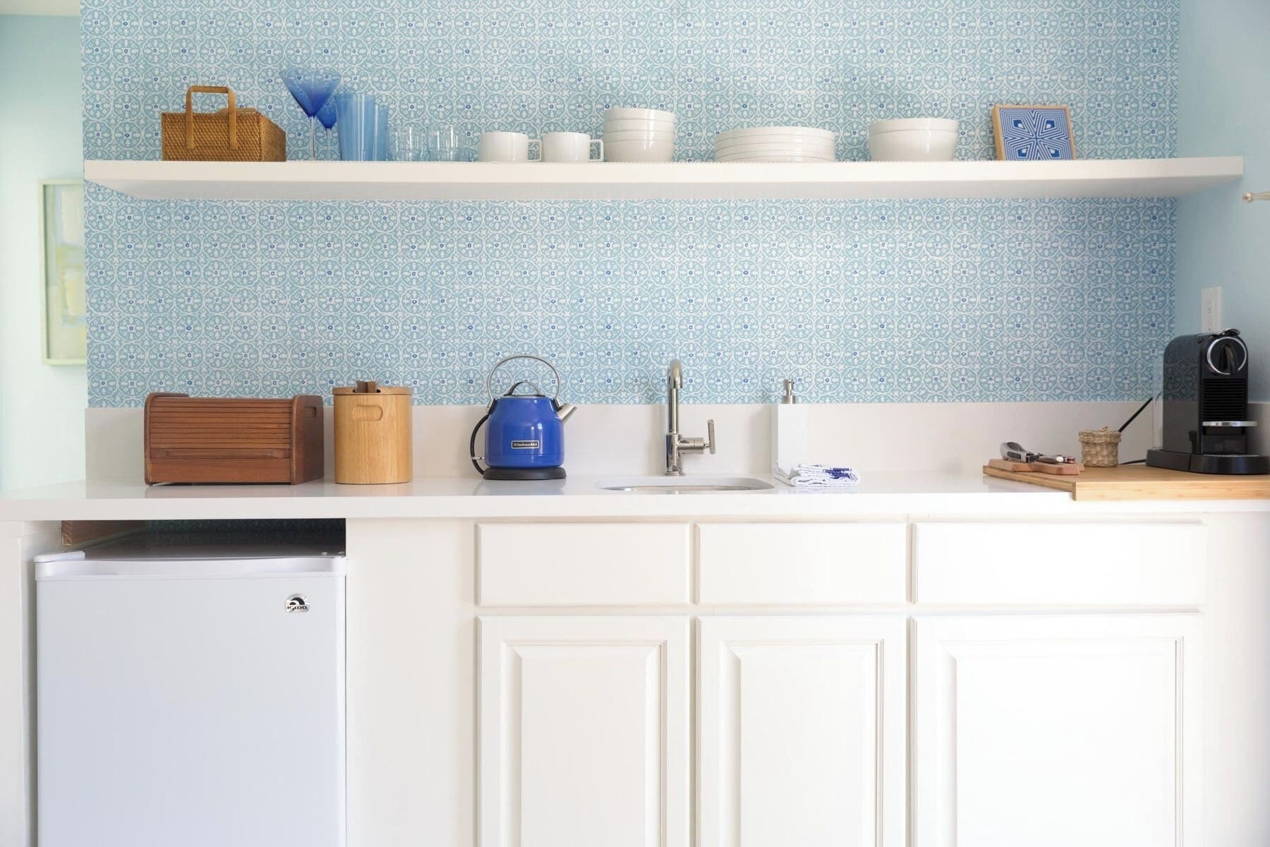Eine Küche mit weißen Schränken, einem weißen Kühlschrank und einer blaue Musterküchenrückwand.