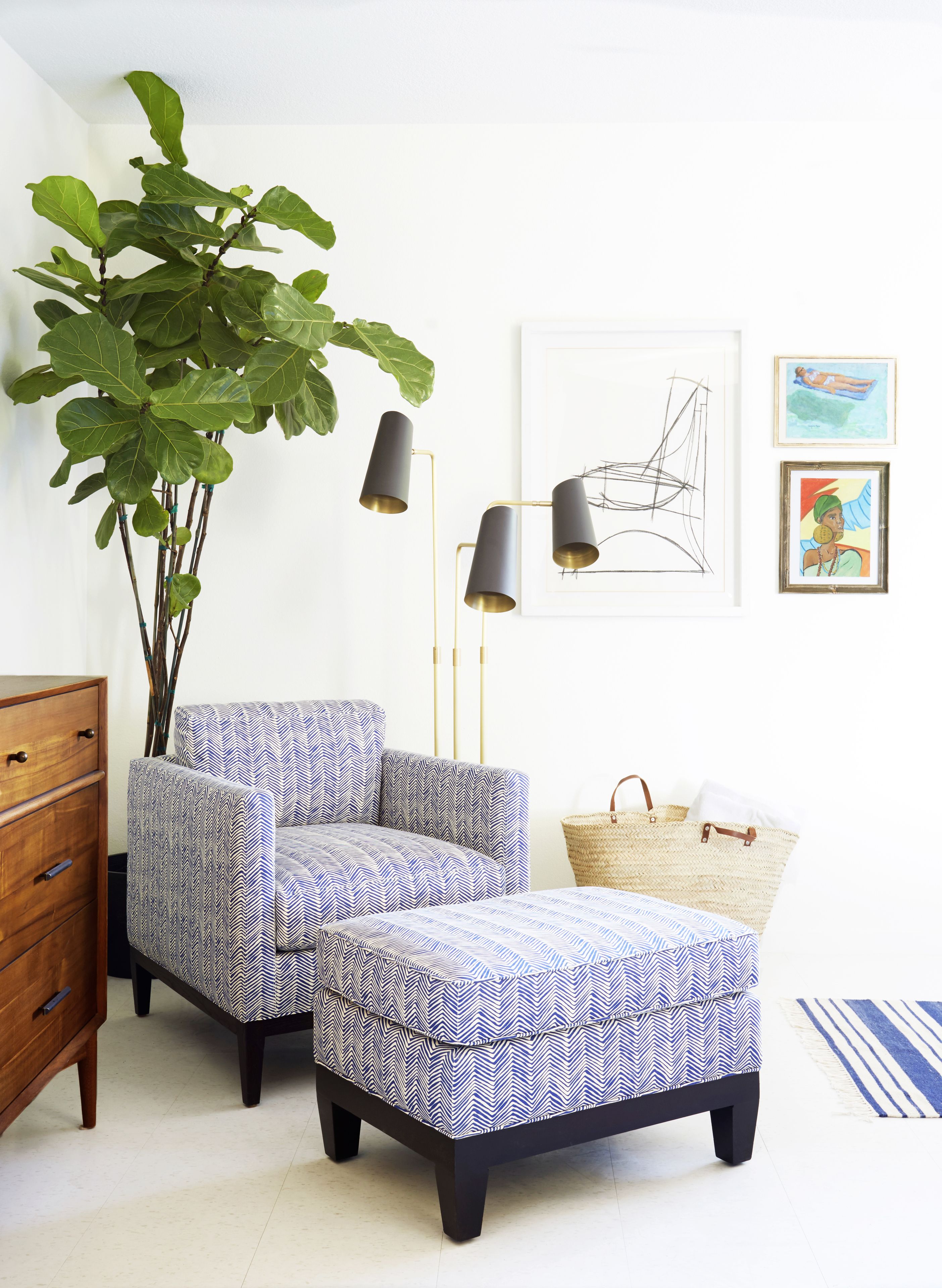 A modern living room with a sofa and ottoman, a large plant, a floor lamp, and artwork on the wall.