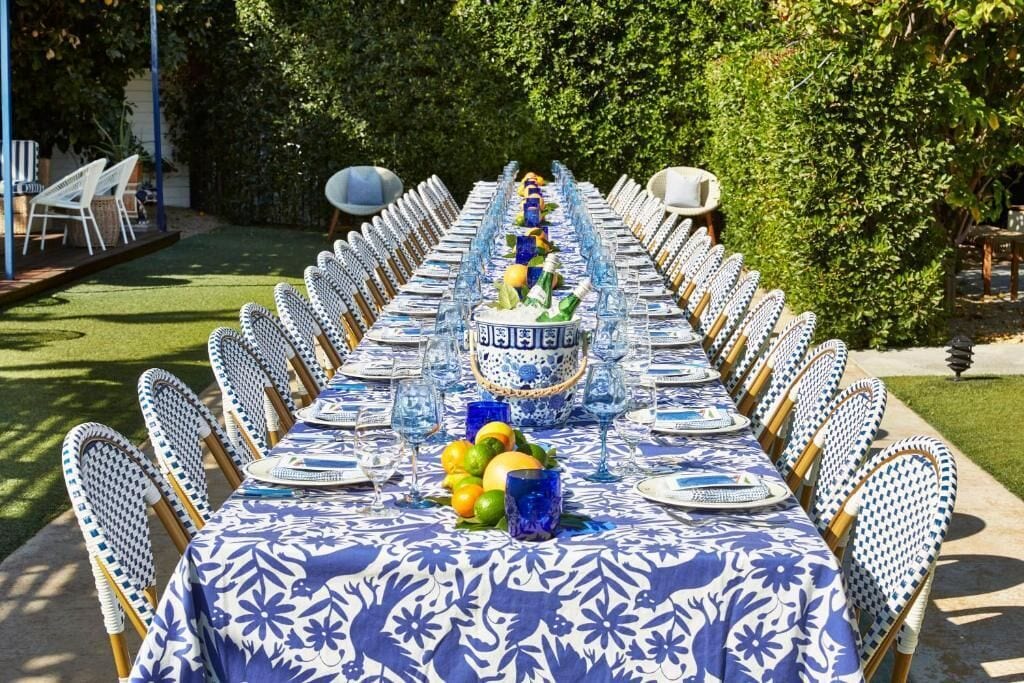 An outdoor dining area with a long table set for a meal, surrounded by chairs.
