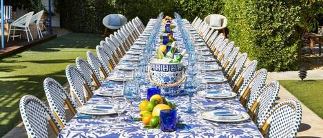 An outdoor dining area with a long table set for a meal, surrounded by chairs.