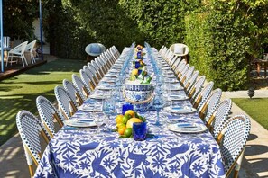 An outdoor dining area with a long table set for a meal, surrounded by chairs. - Holiday House Palm Springs (Palm Springs)
