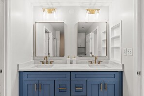 Un baño con dos lavamanos, un espejo grande y armarios azules.