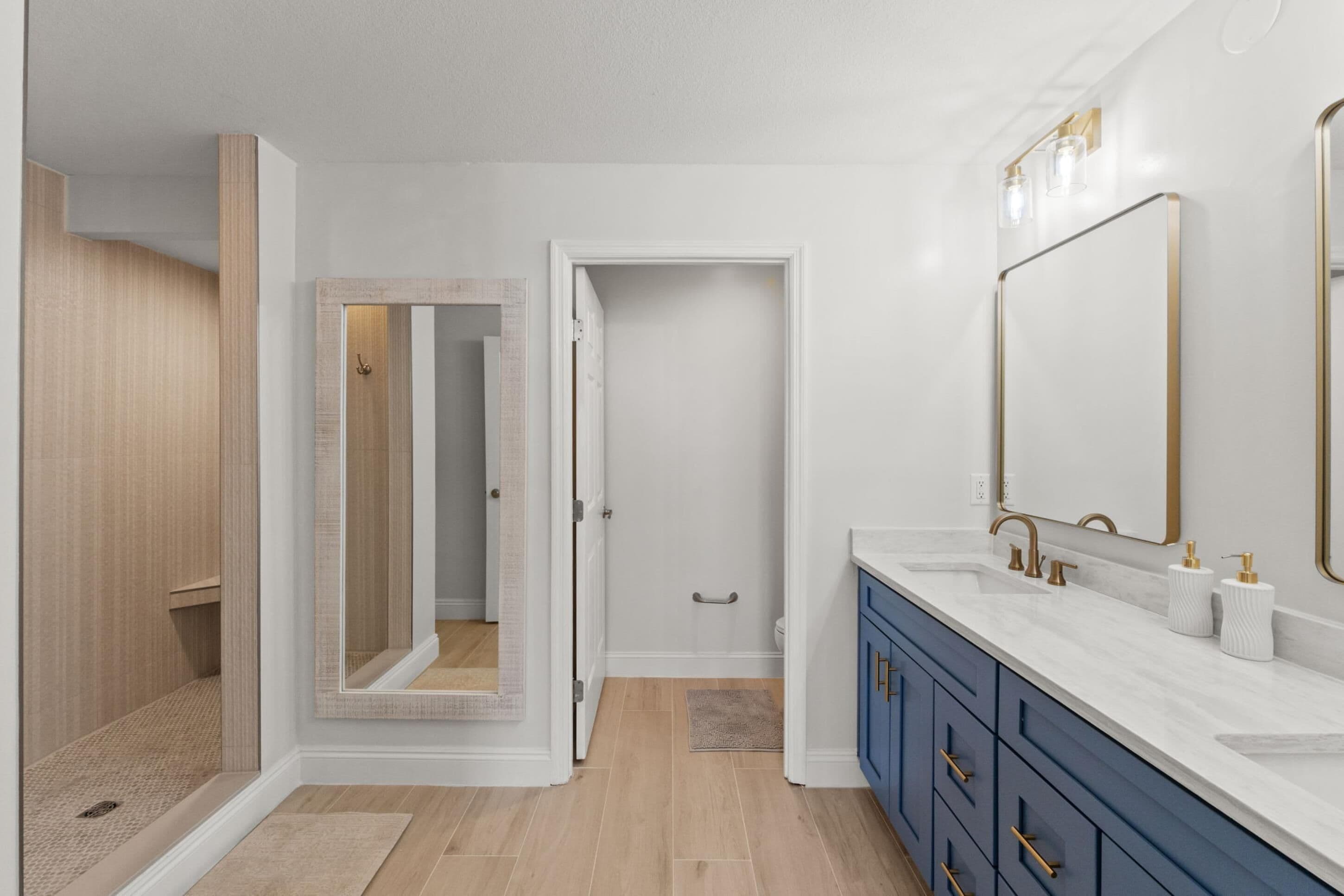 A modern bathroom with a large mirror, a walk-in shower, and a vanity with a sink and cabinet.