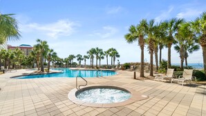 Zona de piscina con jacuzzi, palmeras y sillas de descanso.