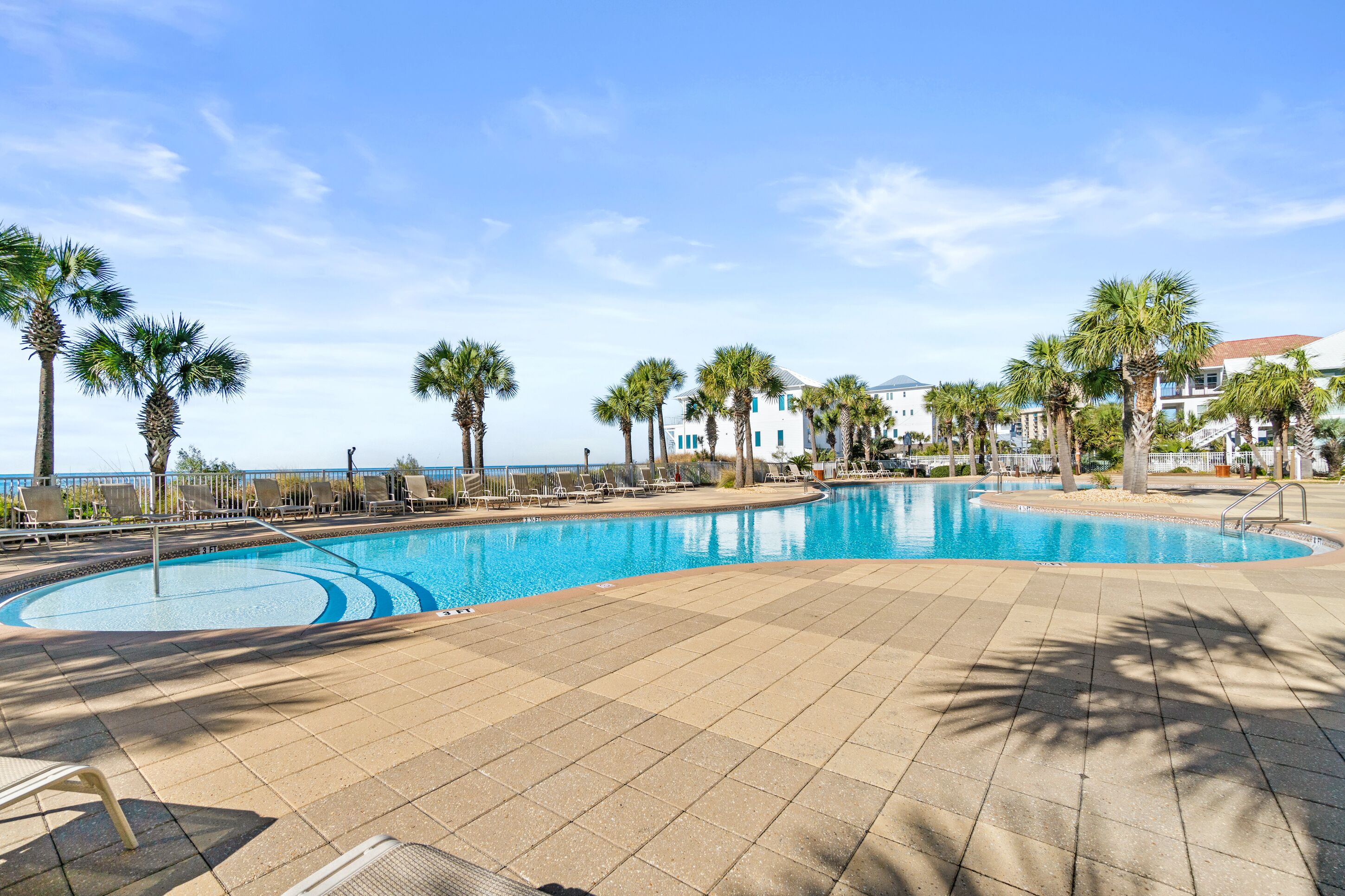Ein Swimmingpool mit Liegestühlen und Palmen, umgeben von Gebäuden.