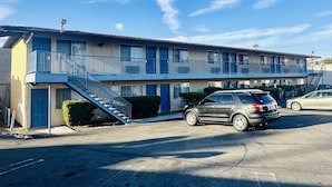 Un motel de dos pisos con fachada azul, un área de estacionamiento techada y una escalera que conduce a la entrada.