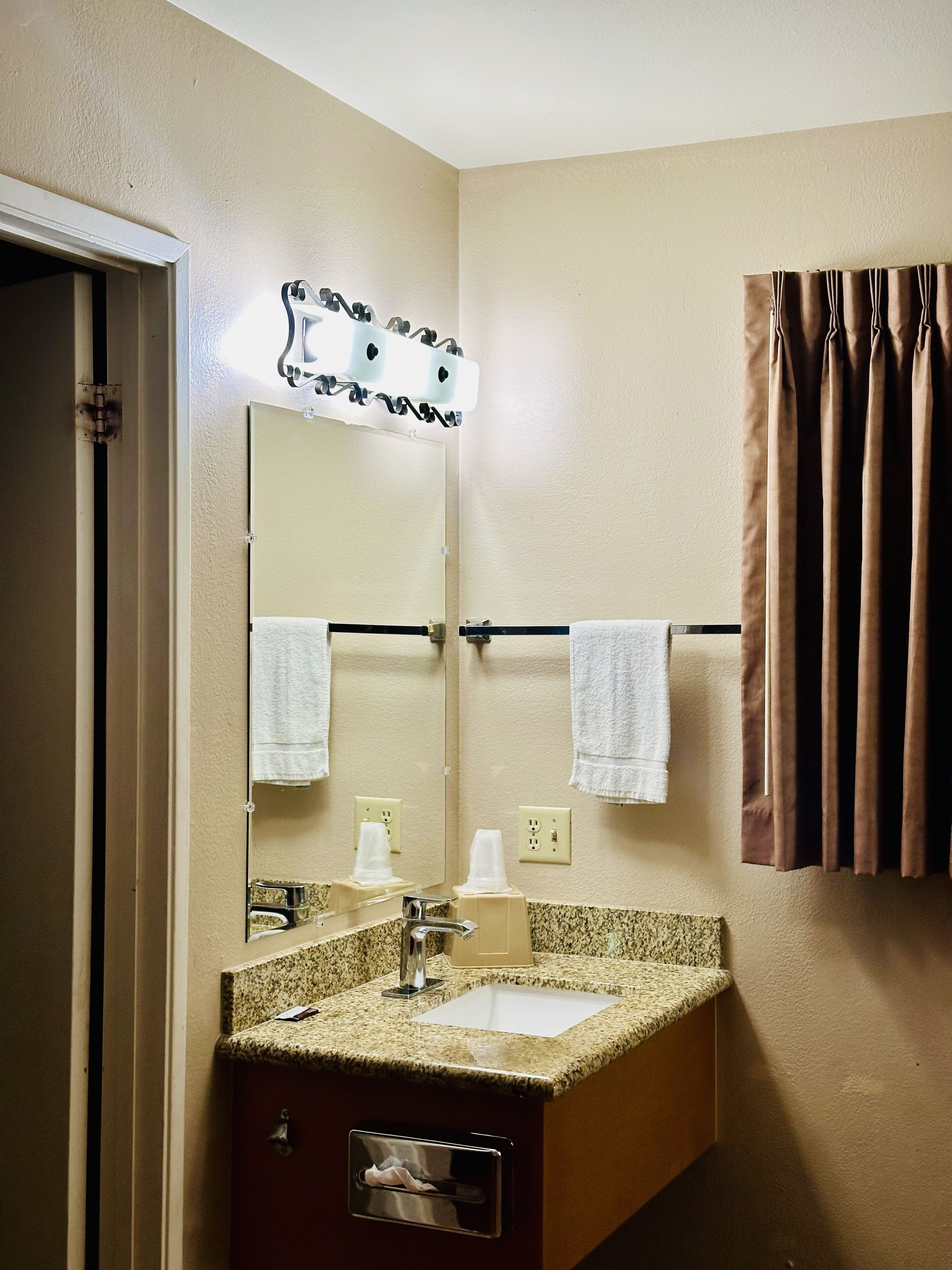 A hotel bathroom with a granite countertop sink, a mirror, two towels, a towel rack, and a curtain.