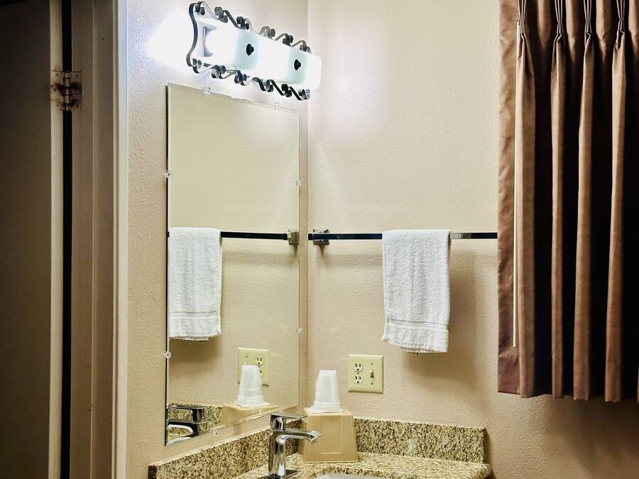 A hotel bathroom with a granite countertop sink, a mirror, two towels, a towel rack, and a curtain.