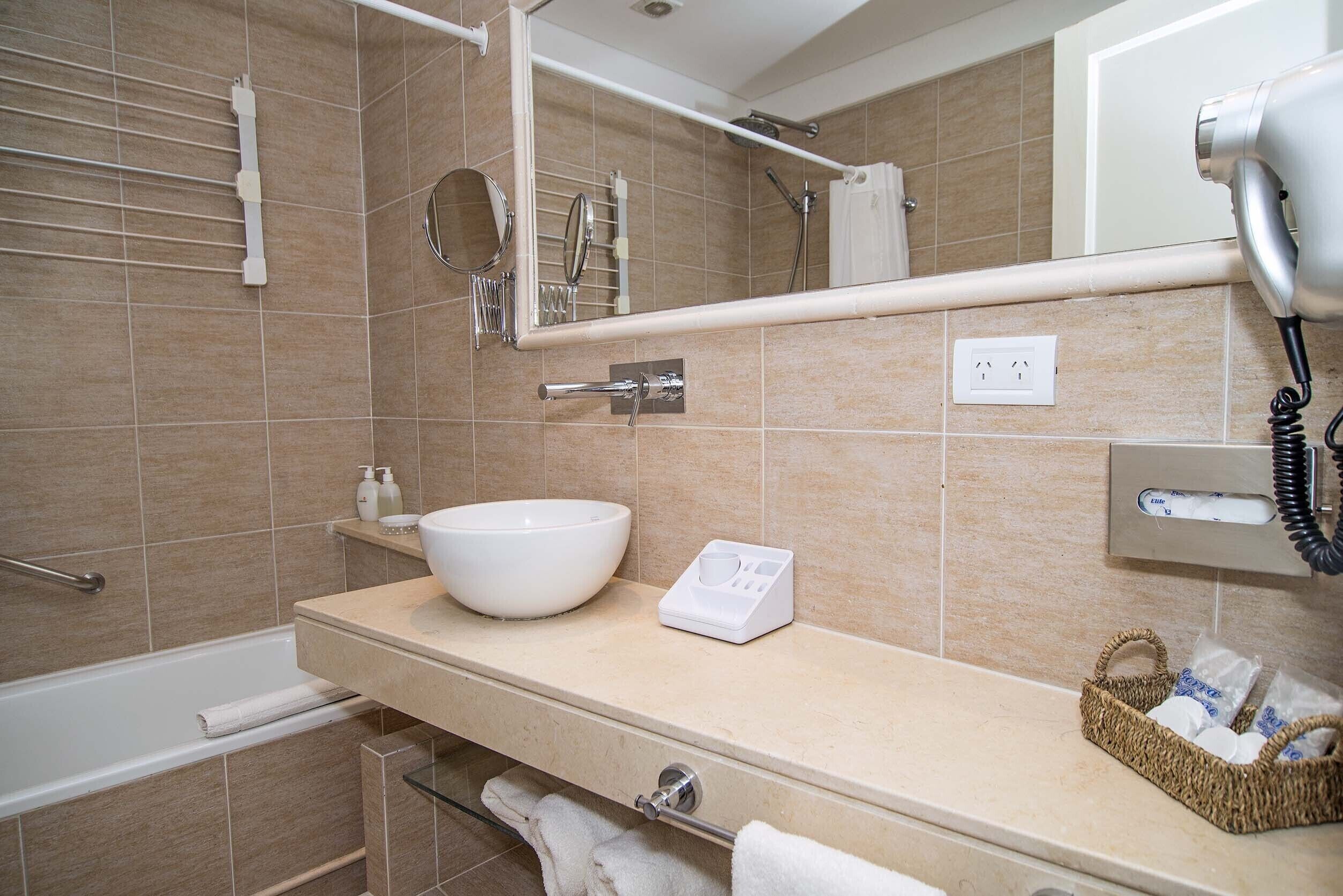 A modern bathroom with a large sink, a mirror, a towel rack, a shower area, and a hairdryer.