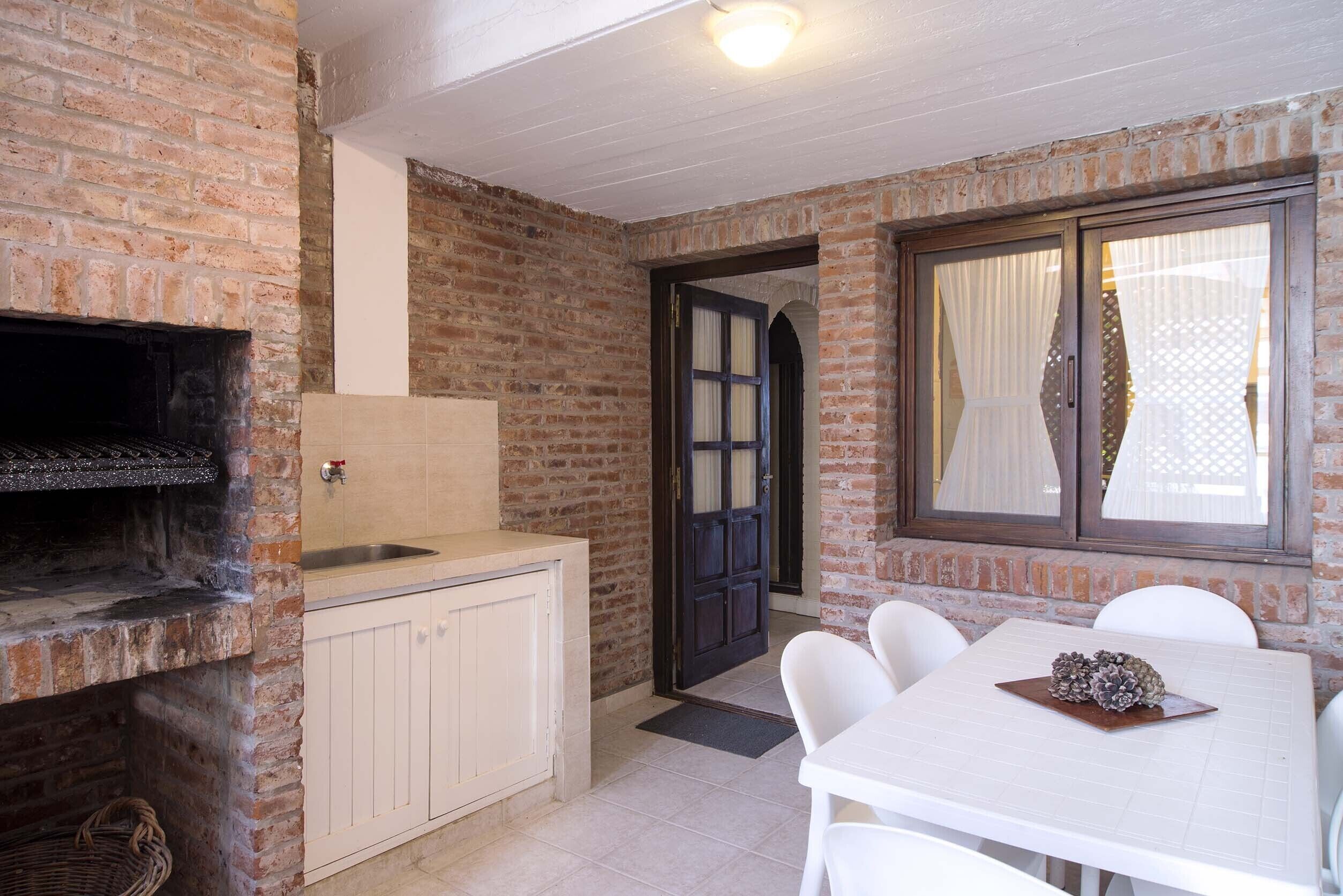 A rustic kitchen with a brick wall, a built-in oven, a sink, and a dining area with a table and chairs.