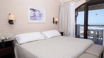 A hotel room with a bed, two bedside lamps, a phone, a framed picture, and a balcony with a view of the sea.
