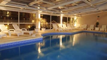 Una piscina interior con sillones de descanso y plantas en macetas.