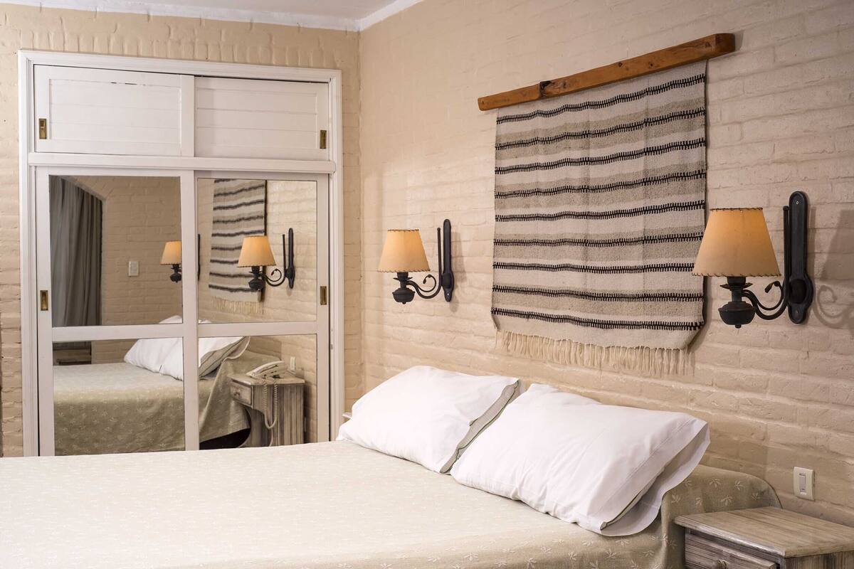 A hotel room with a bed, a wardrobe, a mirror, and two wall-mounted lamps.