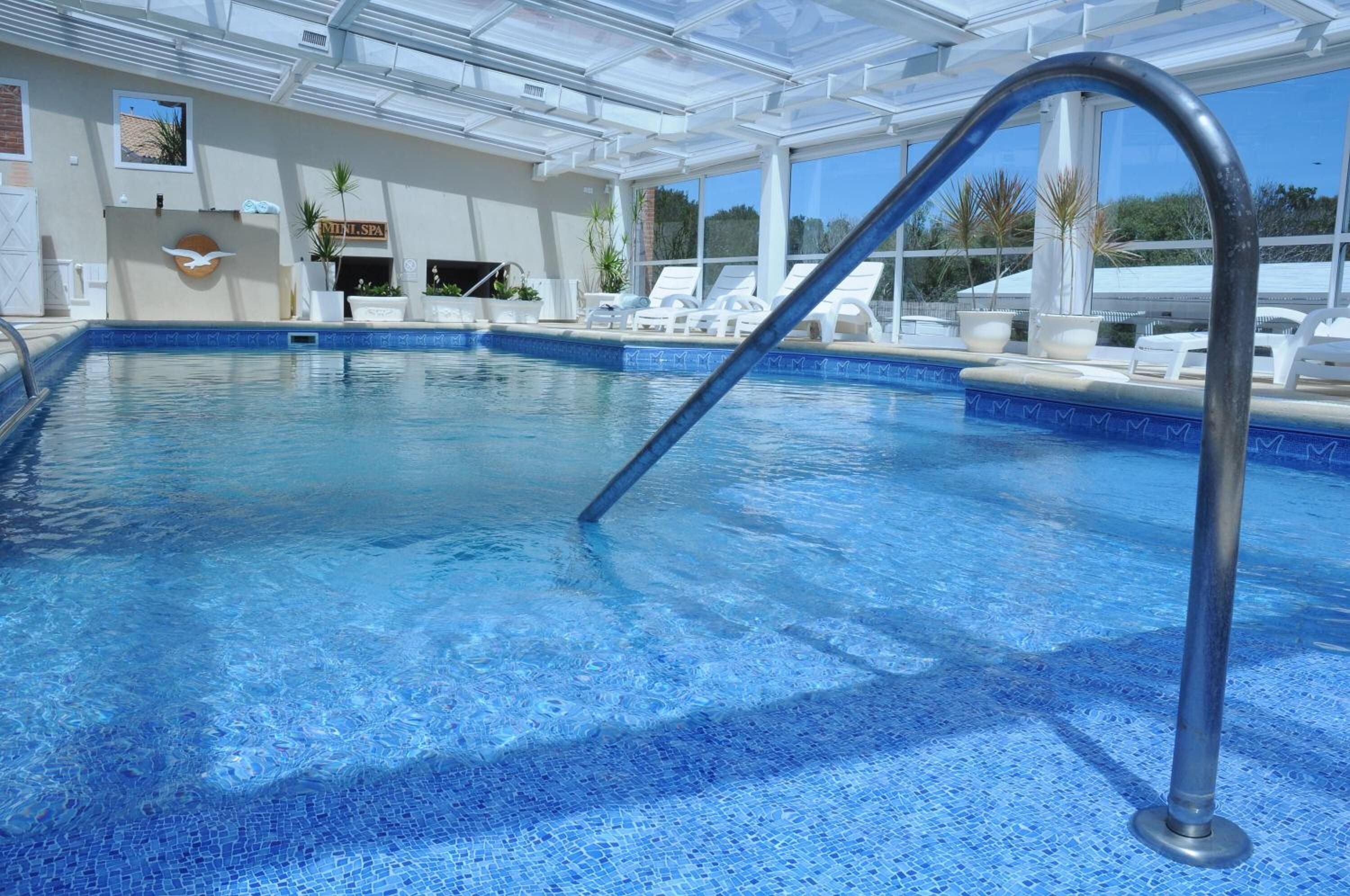 Ein Swimmingpool mit blauem Mosaikboden, einer Metallleiter und Liegestühlen rund um das Becken.