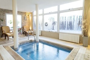 A spa pool area with a stone wall, two chairs, and a large window with a view of palm trees. - Carilo Soleil Apart Hotel (Carilo)