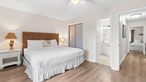 Een slaapkamer met een bed, nachtkastje, lamp, plafondventilator en een badkamer zichtbaar door een open deur.