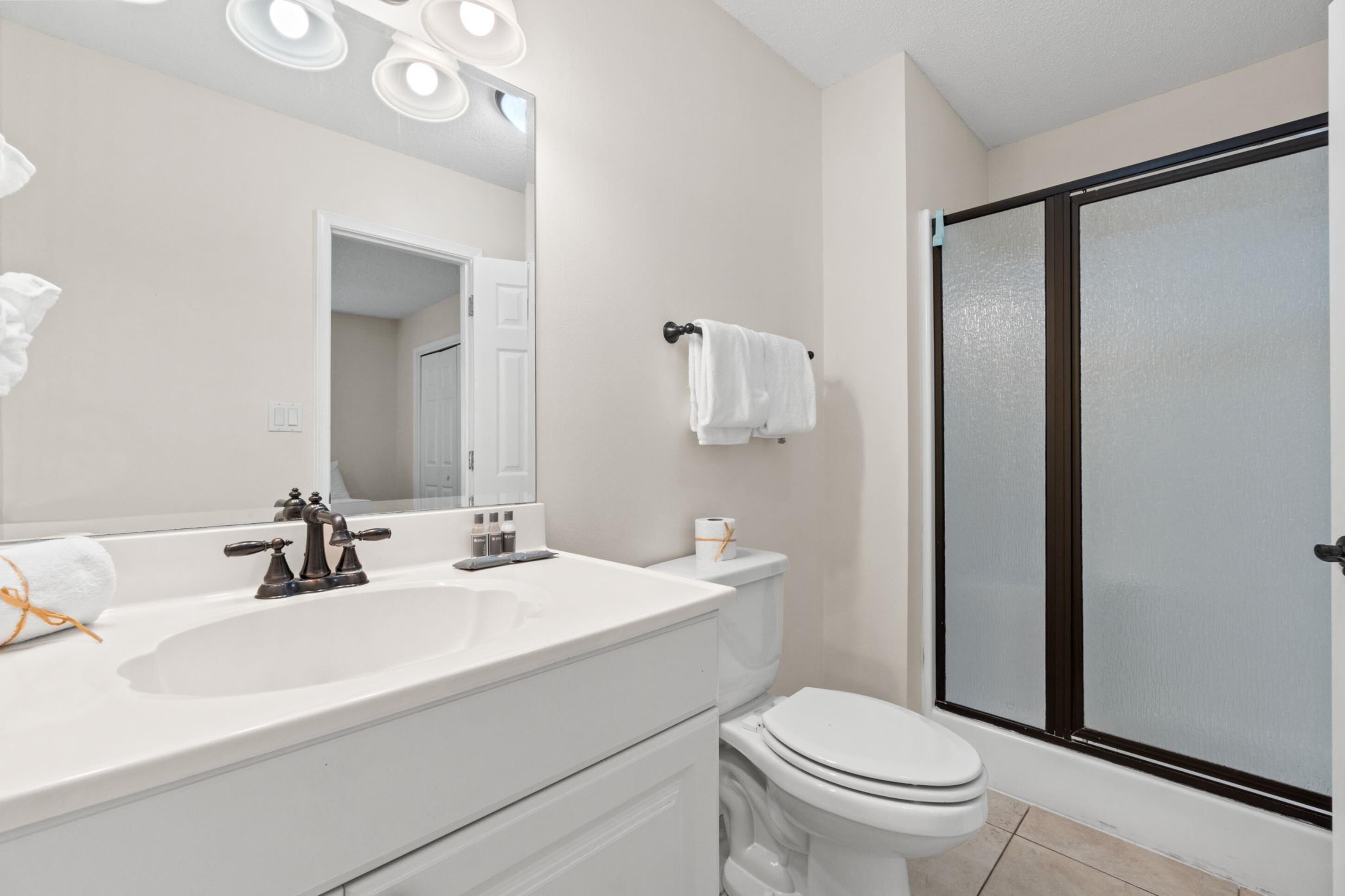 A bathroom with a white sink, a mirror, a toilet, and a shower with frosted glass doors.