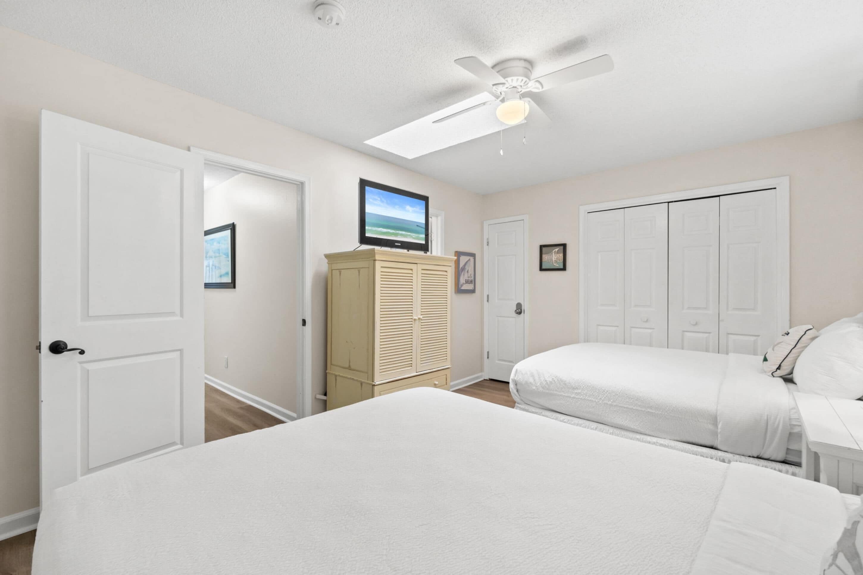 A bedroom with two beds, a ceiling fan, a TV, and a wardrobe.