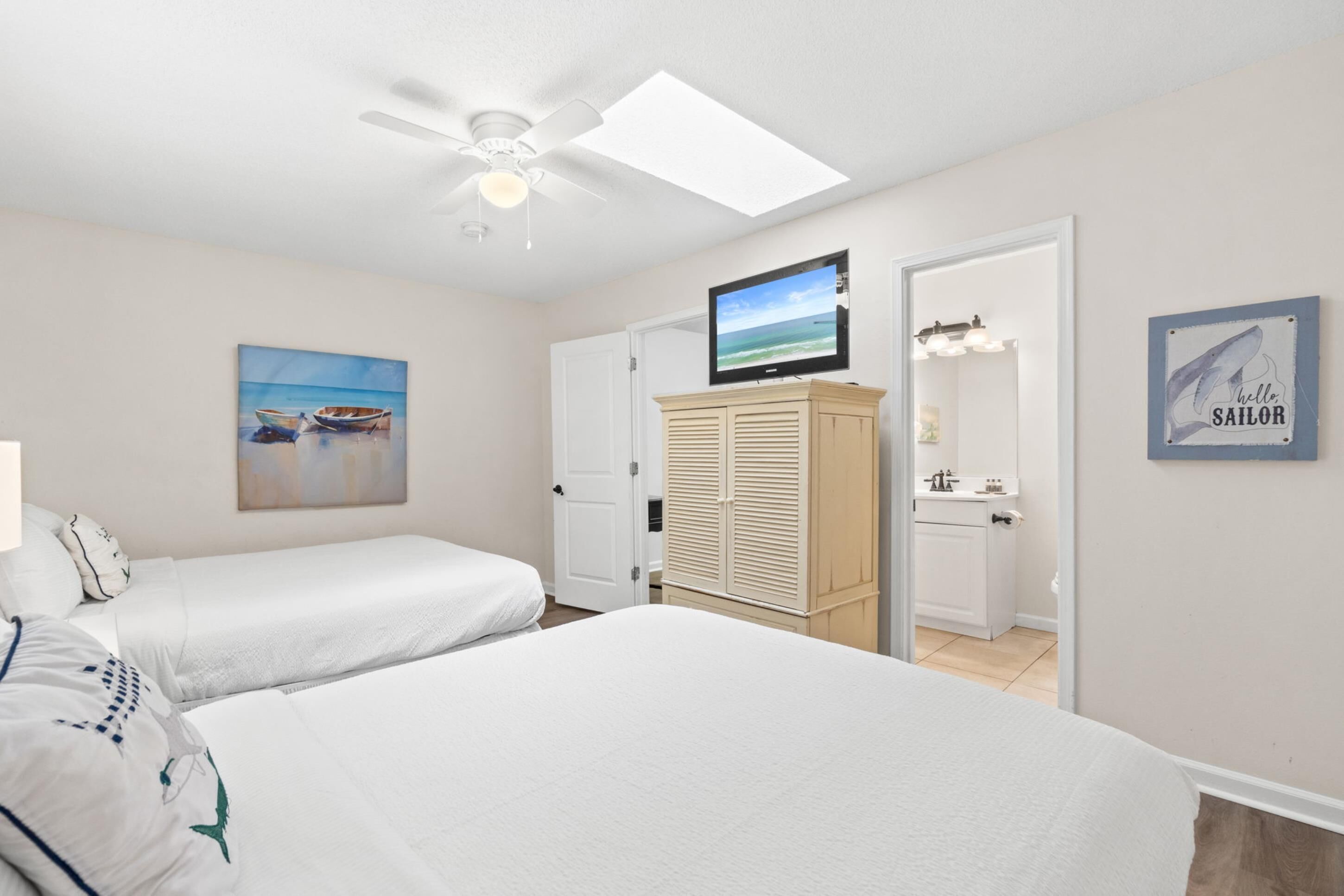 A bedroom with two beds, a ceiling fan, a TV, a wardrobe, and a painting.