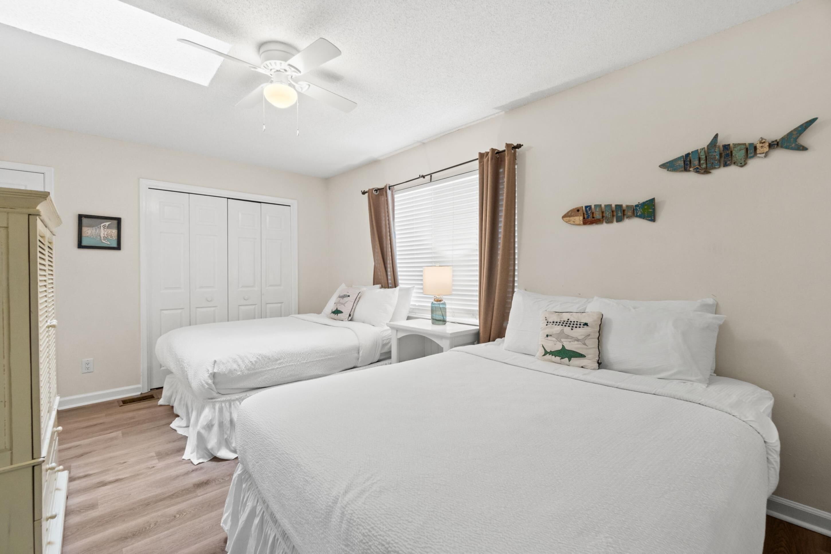 Ein Schlafzimmer mit zwei Betten, einem Deckenventilator, einem Fenster mit Vorhängen und einer Wanddekoration mit Fischmotiven.